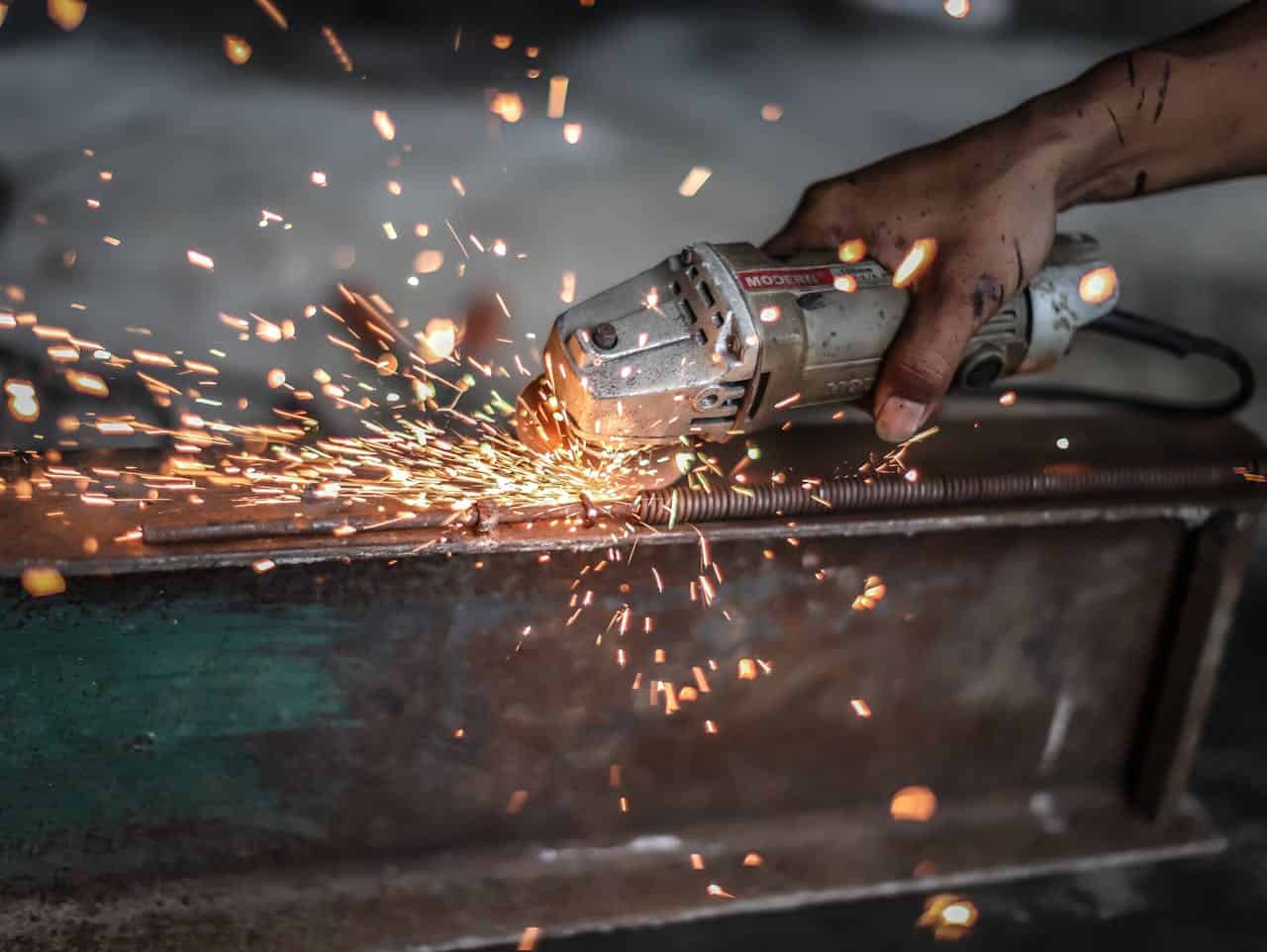our-services-2 Close-up of a metalworker using a grinder with sparks flying, showcasing precision and skill.